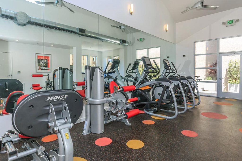 Description: A gym room with exercise machines and mirrors, available for residents of apartments in Hollywood CA.