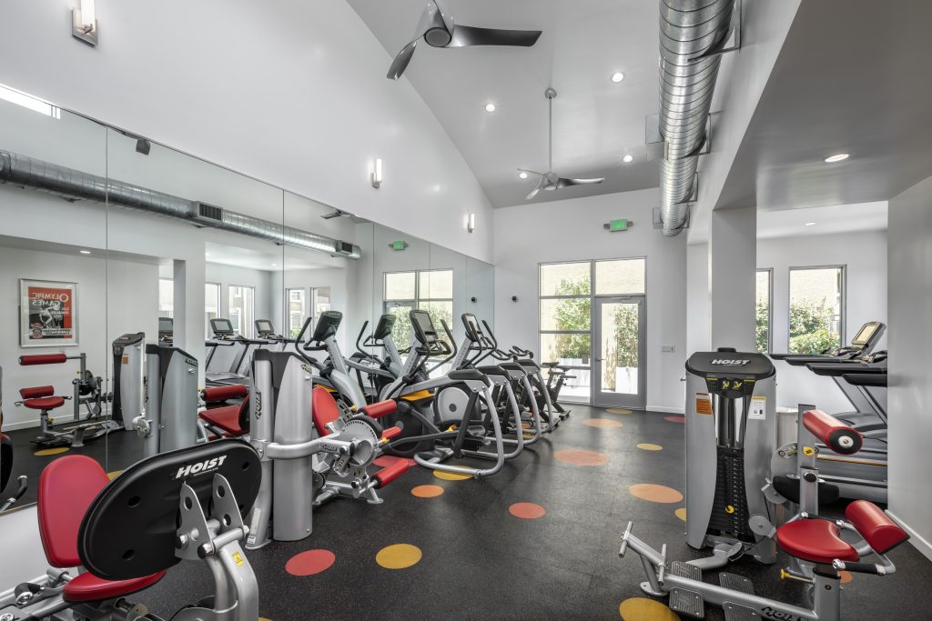 A gym equipped with exercise machines and a fan, conveniently located within an apartment complex in Hollywood, CA.