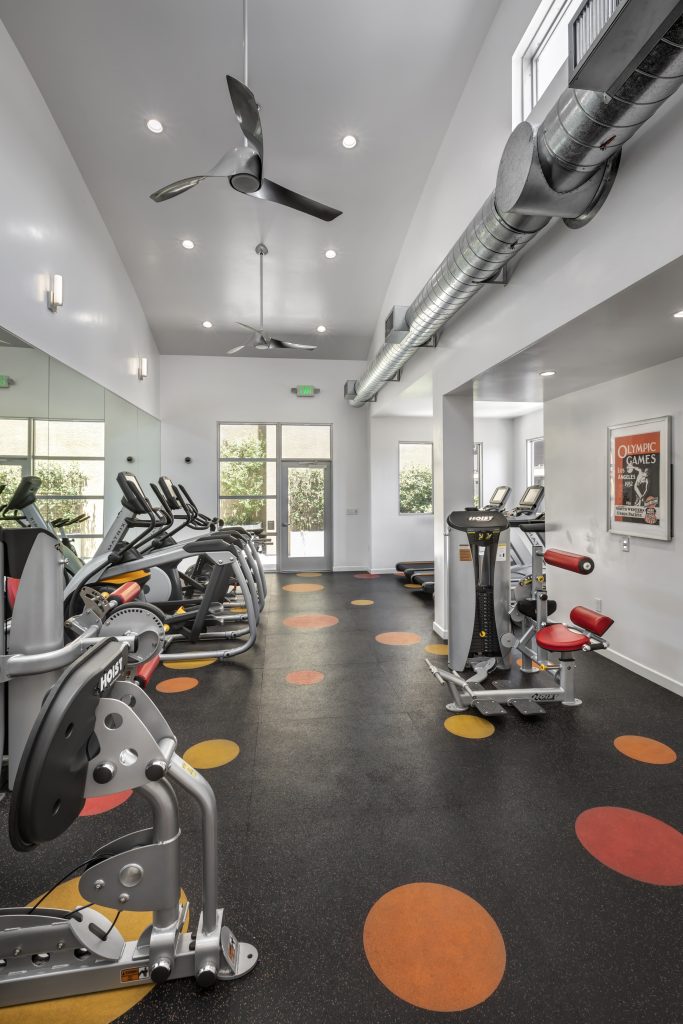 A gym with exercise machines and a ceiling fan, conveniently located near apartments for rent in Hollywood CA.