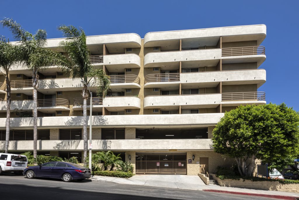 An apartment building in Hollywood CA with balconies and palm trees, offering apartments for rent.